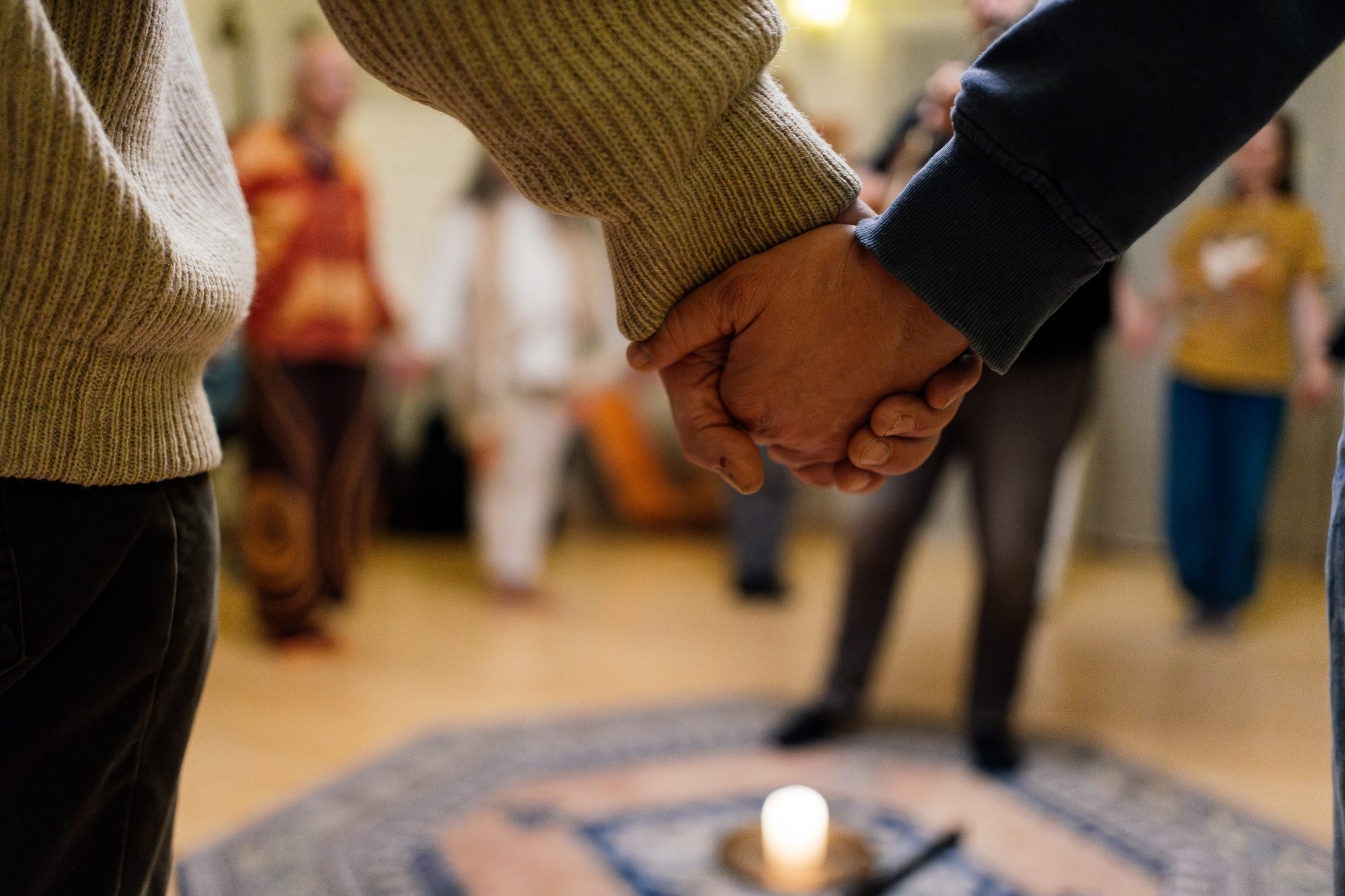 Menschen stehen im Kreis und halten sich an den Händen, in der Mitte brennt eine Kerze
