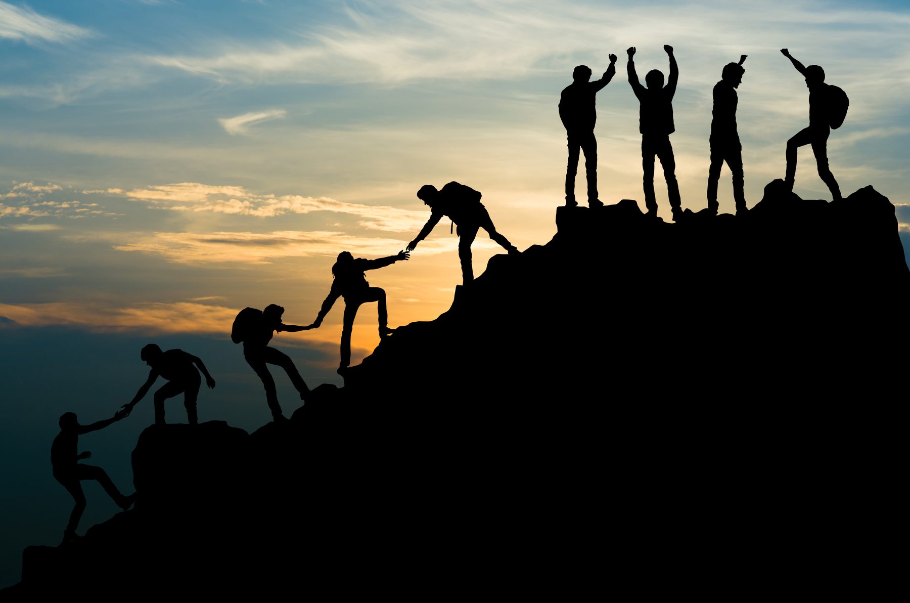 Silhouetten von Menschen, die sich gegenseitig auf einen Berggipfel helfen