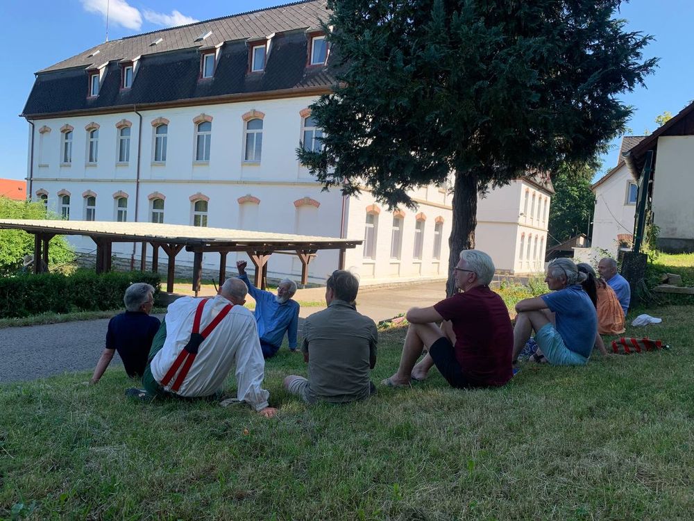 Eine Gruppe sitzt im Gras vor einem großen Haus im Gespräch